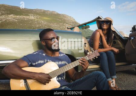 Divers couples prenant une pause au bord de la route le jour ensoleillé à côté du cabriolet voiture l'homme jouant de la guitare Banque D'Images