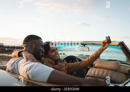Divers couple assis dans une voiture convertible et de prendre un selfie Banque D'Images