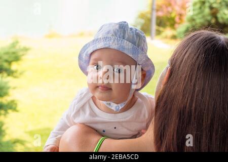 Bébé bleu dans un chapeau reposant sur l’épaule de la jolie mère, portrait du visage du bébé en gros plan Banque D'Images