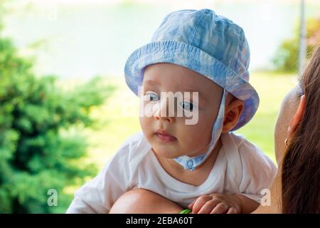 Portrait intelligent de l'expression du visage du nourrisson, bébé en casquette sur la petite tête avec un visage fasciné et des yeux bleus focalisés Banque D'Images