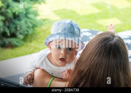 Visage de bébé surpris avec une expression fascinée, petit enfant mignon dans les bras de la mère regarde dehors avec la bouche ouverte et les yeux bleus ouverts de large focalisés Banque D'Images