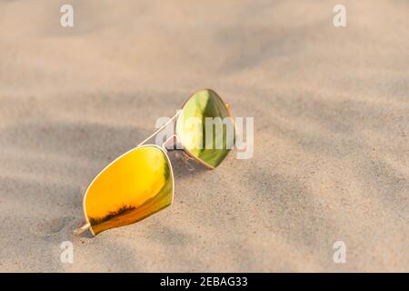 Lunettes de soleil sur la plage reflétant les dunes de sable. Lunettes de soleil miroirs sur la plage de sable en été. Lunettes de soleil sur le sable comme concept de vacances d'été. Banque D'Images