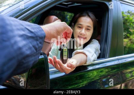 Gros plan du concessionnaire qui donne la clé de la voiture du nouveau propriétaire. Nouvelle voiture. Concessionnaire automobile qui donne la clé d'automobile femme pour l'essai sur route de campagne. Mise au point douce souriante W Banque D'Images