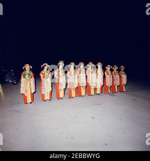 Voyage vers les États de l'Ouest : Honolulu, Hawaï, arrivée à l'aéroport international d'Honolulu, 9:10. Dix femmes (portant des robes rouges et jaunes avec des chapeaux assortis et tenant leis fleur) se posent debout dans une rangée à l'aéroport international d'Honolulu à Honolulu, Hawaï. Banque D'Images