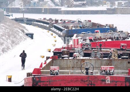 Brunswick, Allemagne. 12 février 2021. Un jogging longe des barges amarrées sur le Mittellandkanal gelé dans le port de Braunschweig. De nombreux navires ont été amarrés pendant plusieurs jours dans le port intérieur de l'ancienne ville hanséatique parce que le Mittellandkanal a gelé, tous les brise-glaces ont été appelés pour garder le Weser exempt de glace. Credit: Stefan Jaitner/dpa/Alay Live News Banque D'Images