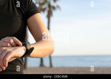 Jeune femme de fitness utilisant la montre intelligente avant ou après la course Sur le fond de la plage avec des palmiers.Sports bien-être et les gens d'athlétisme style de vie conce Banque D'Images