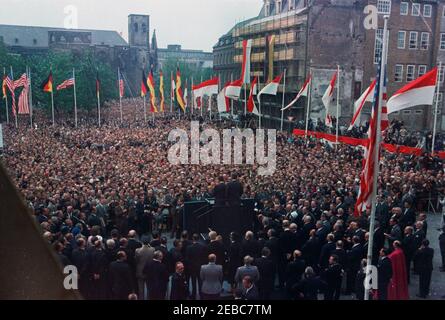 Voyage en Europe: Allemagne, Cologne: Ku00f6lner Rathaus (hôtel de ville), 10:55. Le président John F. Kennedy (debout sur la plateforme Speakersu2019, à la caméra) se prépare à faire des remarques à une foule rassemblée devant Ku00f6lner Rathaus (hôtel de ville) à Cologne, en Allemagne de l'Ouest (République fédérale); Directeur de la radio dans le secteur américain (RIAS) à Berlin et traducteur pour le président Kennedy, Robert Lochner, est à gauche du président. Banque D'Images