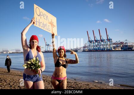 Hambourg, Allemagne. 12 février 2021. Eve Champagne (l), artiste burlesque, et Natalie Warncke tiennent un panneau avec l'inscription 'Open Hotels' et 13 roses blanches avant d'aller nager dans l'Elbe froid près d'Övelgönne avec d'autres baigneurs de glace. Plusieurs dizaines de braves ont plongé dans l'Elbe froid à trois degrés vendredi pour une bonne cause. L'action hebdomadaire des baigneurs de glace vise à encourager les dons pour les sans-abri. Credit: Christian Charisius/dpa/Alay Live News Banque D'Images