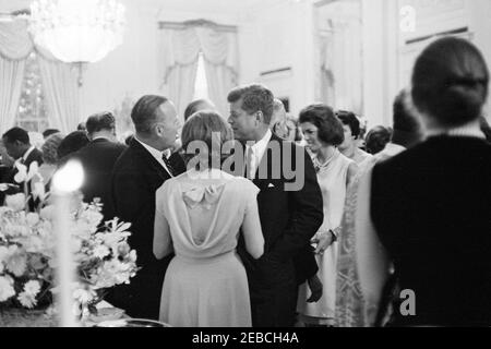 Réception diplomatique, 6:00. Le Président John F. Kennedy (au centre) visite le Secrétaire adjoint à la Défense, Roswell Gilpatric (à gauche), dans la salle de l'est lors d'une réception diplomatique à la Maison Blanche, Washington, D.C. la première dame Jacqueline Kennedy se trouve à droite. Banque D'Images