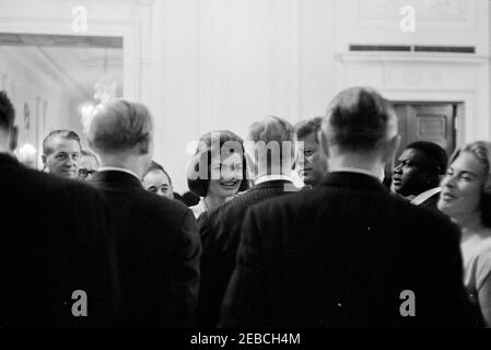 Réception diplomatique, 6:00. Le Président John F. Kennedy (à droite, face cachée) et la première Dame Jacqueline Kennedy (à gauche) la visite avec plusieurs invités non identifiés dans la salle East lors d'une réception diplomatique à la Maison Blanche, Washington, D.C., aide militaire au Président, le général Chester V. Clifton, se trouve tout à gauche. Banque D'Images