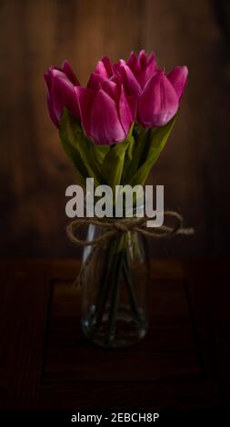 Bouquet de fleurs de tulipe rose dans une bouteille en verre isolée sur fond noir. Banque D'Images