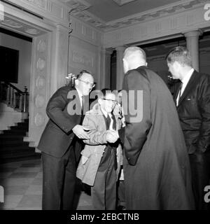 Réception pour l'astronaute John Herschel Glenn, Jr., 11:55. L'astronaute le lieutenant-colonel John H. Glenn Jr. (De retour à la caméra) accueille l'adjoint spécial du président des affaires de sécurité nationale McGeorge Bundy (à gauche) et son fils (qui se serrait la main avec le lieutenant-colonel Glenn), après être arrivés à la Maison Blanche pour une réception en son honneur. Le président John F. Kennedy (à l'extrême droite, face à l'extérieur) regarde dessus; le Grand escalier est visible en arrière-plan à gauche. Hall d'entrée, Washington, D.C. Banque D'Images