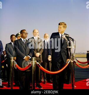 Cérémonies d'arrivée de William Vacanarat Shadrach Tubman, Président du Libéria, 10 h 00. Le président John F. Kennedy prononce des remarques lors des cérémonies d'arrivée de William V.S. Tubman, Président du Libéria. Le Président Tubman (avant, gauche); le Président Kennedy (à micros); le Président des chefs d'état-major interarmées, le général Lyman Lemnitzer (derrière le Président Tubman, partiellement caché); le Secrétaire d'État, Dean Rusk (derrière et à droite du Président Tubman); d'autres non identifiés. Andrews Air Force base, Maryland. Banque D'Images