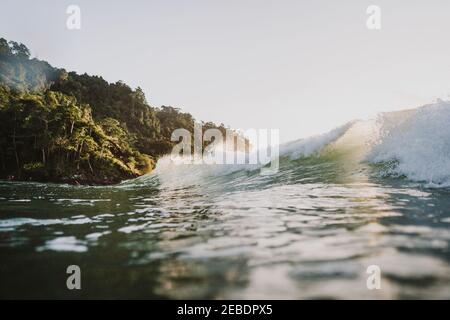 Le soleil brille à travers des vagues écrasant avec des arbres tropicaux en arrière-plan Banque D'Images