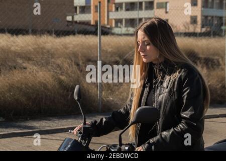 Jolie femme caucasienne portant une veste en cuir avec un tout-noir tenue à côté de sa moto Banque D'Images
