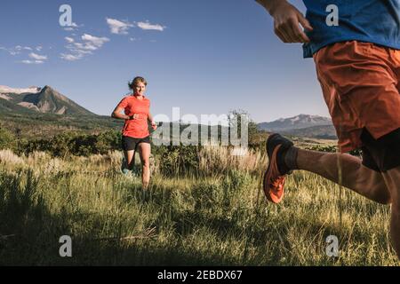 Deux coureurs de sentier parcourent un grand champ d'herbe avec la montagne vue Banque D'Images