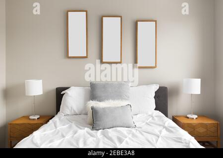 Vue détaillée d'une chambre confortable avec literie blanche et oreillers gris, photos de feuilles au-dessus du lit et lampes sur tables de nuit en bois. Banque D'Images