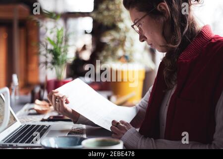 femme d'affaires lit les documents avec ordinateur portable dans le bureau à domicile pendant covid Banque D'Images