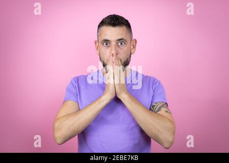 Jeune homme beau portant un t-shirt décontracté sur fond rose choqué couvrant la bouche avec les mains pour erreur. Concept secret. Banque D'Images