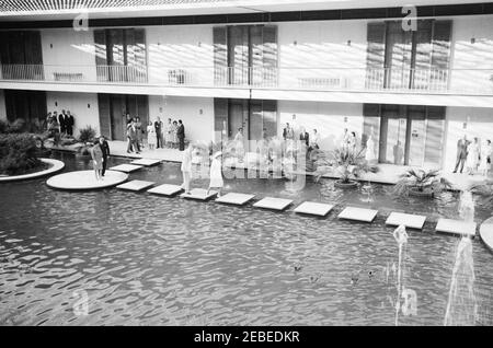 Première dame Jacqueline Kennedyu2019s (JBK) voyage en Inde et au Pakistan: New Delhi, Delhi, Inde, visite à la chancellerie des États-Unis. La première dame Jacqueline Kennedy traverse une piscine sur cour à la chancellerie de l'ambassade des États-Unis à New Delhi, en Inde. L'ambassadeur DES ÉTATS-UNIS en Inde, John Kenneth Galbraith, marche derrière Mme Kennedy; Kitty Galbraith, épouse de l'ambassadeur, se trouve le long du bâtiment à gauche. La première sœur de Ladyu2019s, la princesse Lee Radziwill de Pologne, se trouve sur la pierre circulaire à gauche. Banque D'Images