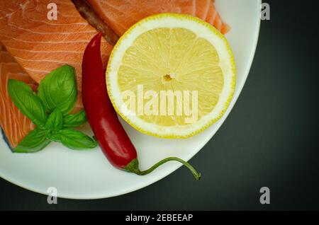 Morceaux de saumon frais vue de dessus plaque blanche. Isolé sur noir. Servi avec du piment, du citron et des verts Banque D'Images