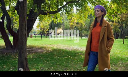 femme heureuse dans une tenue d'automne élégante se promenant dans le parc avec main dans la poche Banque D'Images