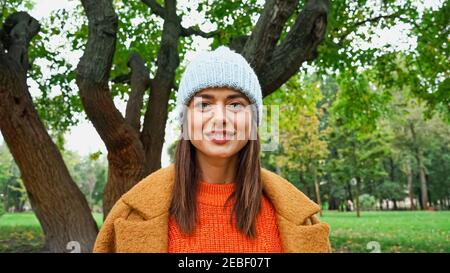 femme joyeuse dans des vêtements élégants regardant l'appareil photo en automne stationnement Banque D'Images