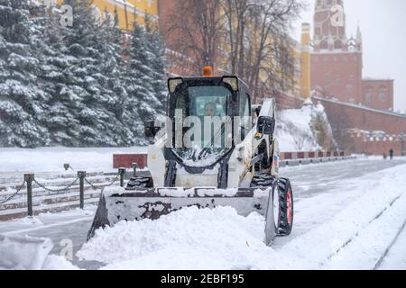 Moscou. Russie. 12 février 2021. Un petit bobcat de pelle-chargeuse enlève la neige du trottoir près des murs du Kremlin lors d'une forte chute de neige Banque D'Images