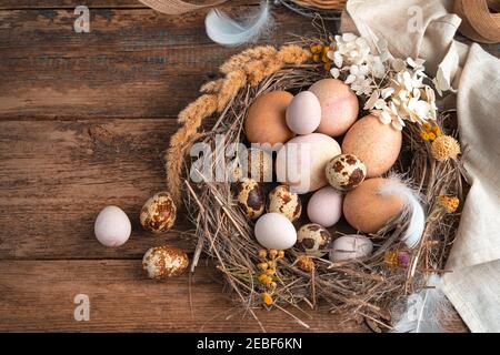 Arrière-plan rétro de Pâques. Les œufs de caille et les œufs de poulet sont dans un nid en osier, décoré de fleurs et de plumes. Banque D'Images