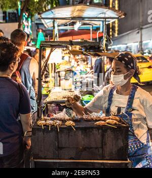 Un cuisinier prépare des brochettes de viande grillée dans un restaurant au marché nocturne de Patong à Bangkok, en Thaïlande.