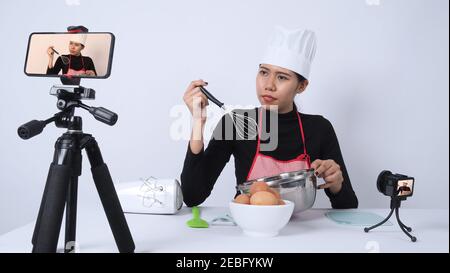 Blogueur de nourriture. Asian femme chef streaming en direct. Elle communique avec les abonnés par téléphone caméra en ligne. Enregistreur de données et en ligne influenceur enregistrement Banque D'Images
