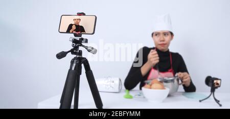 Blogueur de nourriture. Asian femme chef streaming en direct. Elle communique avec les abonnés par téléphone caméra en ligne. Enregistreur de données et en ligne influenceur enregistrement Banque D'Images