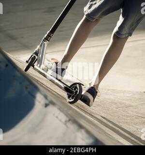 Vue rapprochée de tennager's pieds de la trottinette fait des tours sur un half pipe. Quartier branché de jeunes patineurs bénéficiant d'extérieur au skatepark avec scooter de coup Banque D'Images