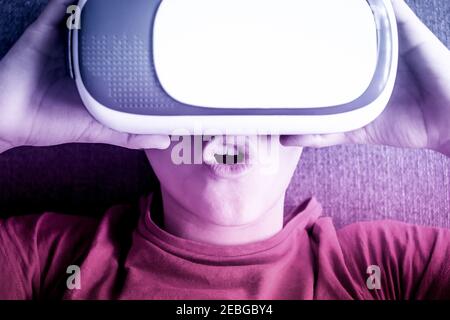 Jeune homme s'amuser avec la technologie de lunettes de réalité virtuelle posée sur le canapé à la maison. Un garçon étonné gestialise le port d'un casque vr. Tech, des vies modernes Banque D'Images