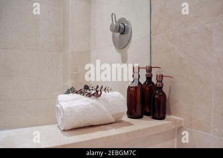 Bouteilles de shampooing en verre ambré avec distributeurs de pompe en acier cuivre dans un spa et une douche en marbre luxueux. Banque D'Images