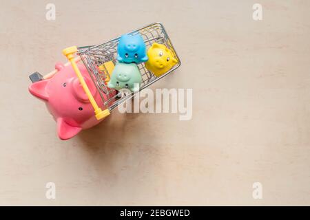 Grande banque de cochons tenant un panier avec des petits bancs de cochons sur fond de bois. Une grande banque de porcs roulant trois banques de porcelets dans un chariot. Banques de cochons i Banque D'Images