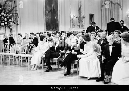 Dîner en l'honneur d'Andru00e9 Malraux, ministre d'État aux Affaires culturelles de France, 8 h 00. Le Président John F. Kennedy et d'autres se réunissent dans la salle est pour assister à un spectacle musical lors d'un dîner en l'honneur du Ministre d'État aux Affaires culturelles de France, Andru00e9 Malraux. Le président Kennedy (au centre à gauche) visite la femme de la ministre, la pianiste Madeleine Malraux; la première dame Jacqueline Kennedy (à droite) visite la ministre Malraux. L'ambassadeur de France aux États-Unis, Hervu00e9 Alphand, et sa femme, Nicole Alphand, sont assis devant la ligne (à l'extrême droite). Également en photo : Directeur du Banque D'Images