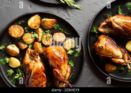 Carcasses de cailles grillées avec pommes de terre sur plaque sur fond de pierre noire. Vue de dessus, plan d'installation, gros plan Banque D'Images