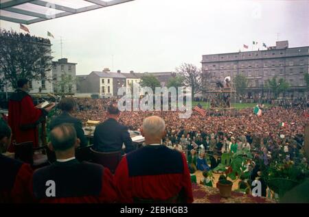 Voyage en Europe: Irlande, Galway: Président Kennedy à Eyre Square, remarques et départ, 11:55. Le maire de Galway, Alderman Patrick D. Ryan (à l'extrême gauche, au pupitre), prononce des remarques devant la foule rassemblée à Eyre Square à Galway, en Irlande, lors d'une cérémonie de bienvenue pour le président John F. Kennedy. Le président Kennedy (assis à l'arrière de la caméra, à droite du maire) et d'autres invités distingués s'assoient sur la plate-forme supérieure; A droite du lectre (sur la table) se trouve le cercueil et le rouleau doré présentés au Président, dans le cadre de la cérémonie, lui accordant la liberté d'honneur du Banque D'Images
