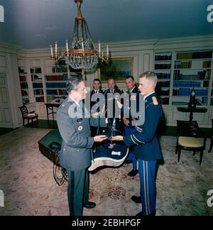 Funérailles d'État du président Kennedy: Des membres du 3e Régiment d'infanterie des États-Unis (la vieille garde) présentent la caparison noire Jacku2019s (selle, bride, couverture, épée, bottes et éperons) à l'aide militaire adjointe, le lieutenant-colonel James M. Connell. Les membres du 3e Régiment d'infanterie des États-Unis (la vieille garde) livrent à la Maison Blanche la selle, la bride, la couverture, l'épée, les bottes et les éperons de u0022Black Jack,u0022 le cheval sans rebord de la procession funéraire du président John F. Kennedy. En premier plan, le soldat de première classe Arthur A. Carlson (à droite) présente une chaussure à l'aide militaire adjointe, le lieutenant Colon Banque D'Images