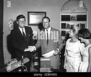 Visite de Stan Musial, joueur de la Ligue majeure de baseball (MLB) pour les Cardinals de Saint-Louis, et de la famille, 4:10. Le président John F. Kennedy tremble la main avec Stan Musial (au centre), joueur de la Ligue majeure de baseball (MLB) pour les Cardinals de St. Louis, lors d'une visite dans le Bureau ovale. Sa femme, Lillian Musial, et sa fille, Janet Musial, regardent de droite. White House, Washington, D.C. Banque D'Images