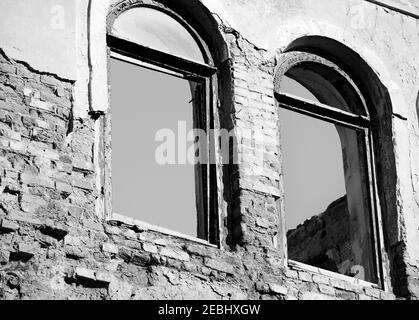 Mur de briques de l'ancienne maison détruite avec des fenêtres cassées. Image en noir et blanc. Banque D'Images