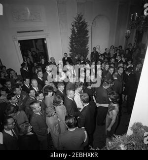 Fête de Noël du personnel de la Maison Blanche dans la salle est, 6:30. Le président John F. Kennedy et la première dame Jacqueline Kennedy (toutes deux au centre à droite, vue d'en haut) accueillent les clients rassemblés à Cross Hall, lors d'une fête de Noël pour le personnel de la Maison Blanche. Les clients remplissent le couloir et la salle verte à gauche. Également en photo : aide de la Force aérienne au président, brigadier-général Godfrey T. McHugh; agent du Service secret de la Maison Blanche, Clint Hill. White House, Washington, D.C. Banque D'Images