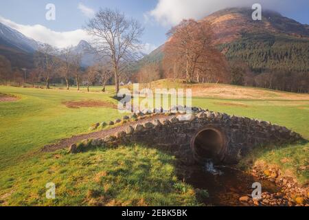 Une vieille passerelle en pierre au-dessus d'un ruisseau sur un parcours de golf public près de Ballachulish, à Glencoe dans les Highlands écossais. Banque D'Images