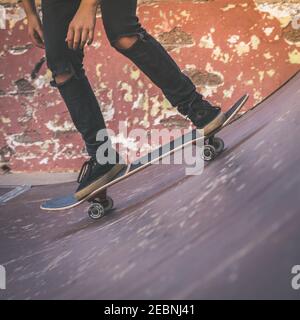 Vue rapprochée de tennager's pieds équitation un skateboard faisant des tours sur demi-lune. Quartier branché de jeunes patineurs bénéficiant d'extérieur au skatepark avec patinage boa Banque D'Images