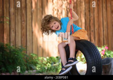 Balançoire pour enfants dans l'arrière-cour. Enfant jouant à l'extérieur. Joyeux mignon petit garçon balançant et avoir amusant en bonne santé des vacances d'été activité. Banque D'Images