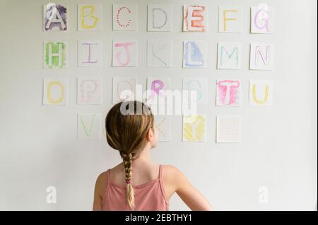 Vue arrière de la fille (8-9) regardant l'alphabet sur le mur Banque D'Images