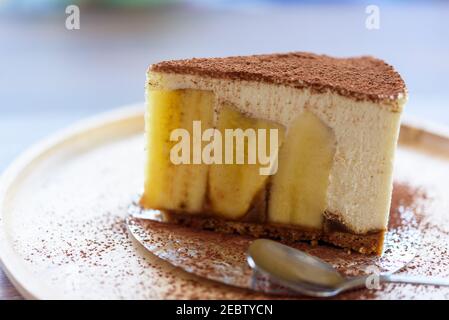 Gros plan sur une assiette en bois avec un gâteau à la banane et de la poudre de chocolat. Mélange de tarte banoffee maison avec craquelins écrasés, banane, crème fouettée au freah, choco Banque D'Images