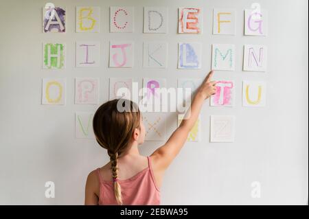 Vue arrière de la fille (8-9) regardant l'alphabet sur le mur Banque D'Images