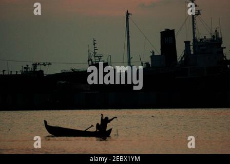 Silhouettes d'une partie d'un navire amarré et d'un pêcheur travaillant avec des filets de poisson d'un bateau flottant sur une piscine intérieure, avant le coucher du soleil dans la zone côtière de Marunda, Jakarta, Indonésie. Banque D'Images